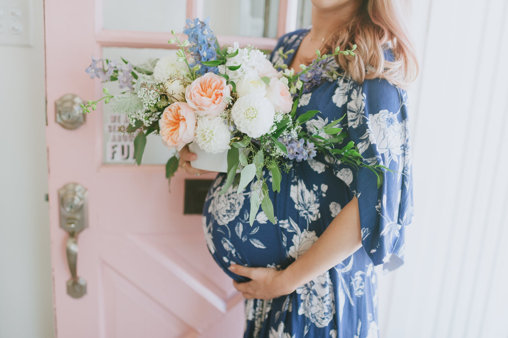 Girl holding flowers with baby bump in front of pink door - Project Nursery