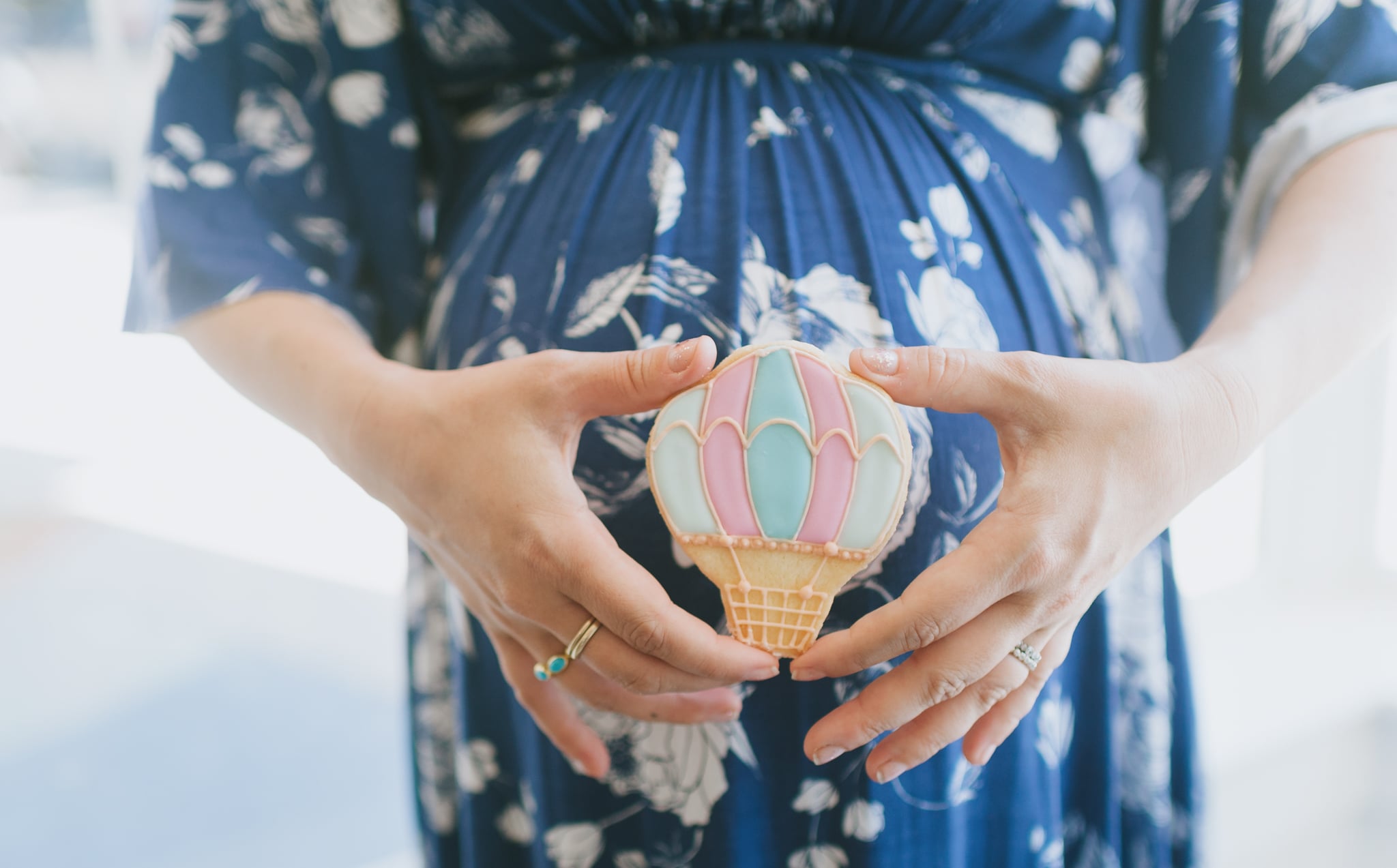 Pink and blue hot air balloon cookie held in front of baby bump